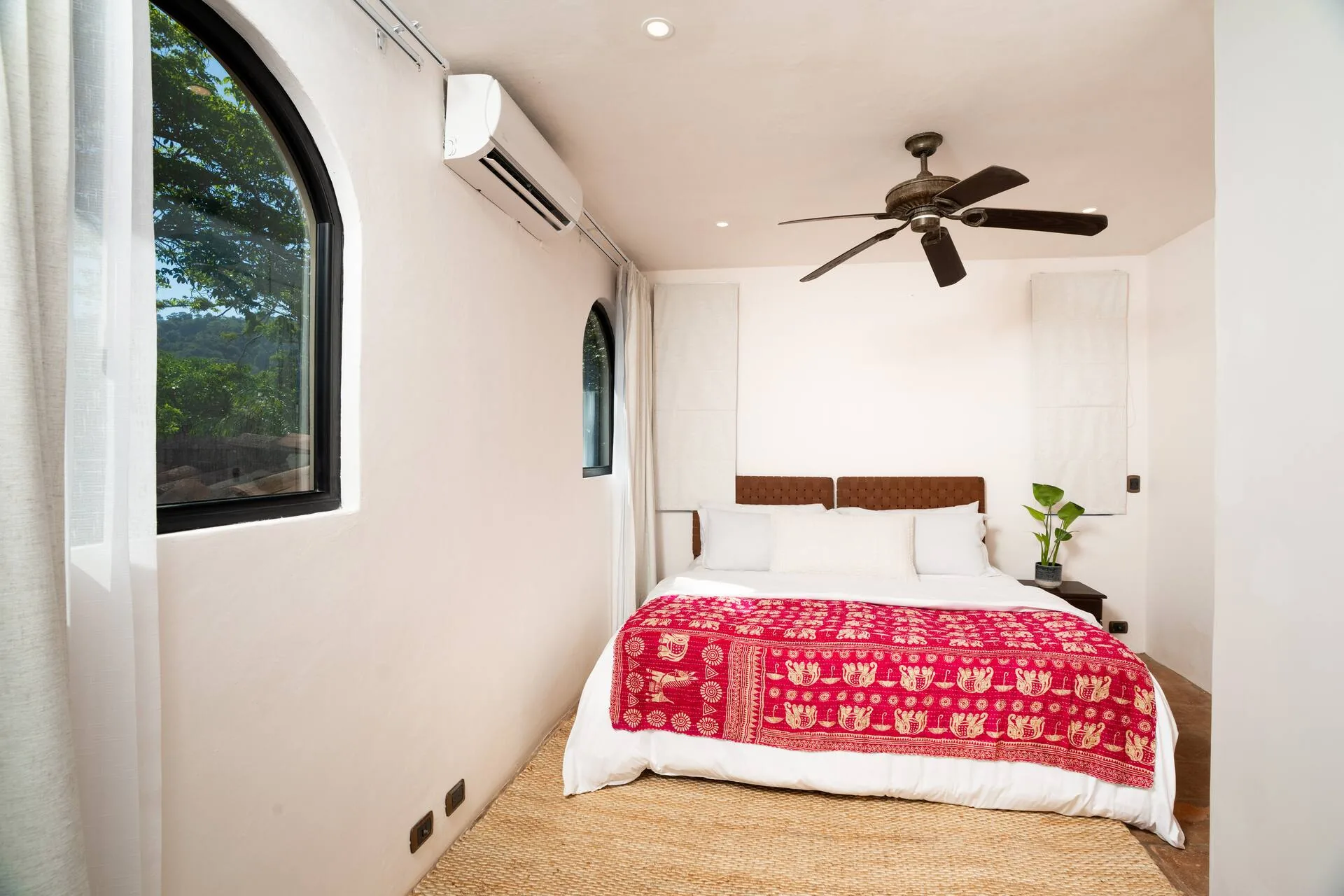 Bedroom with king bed and red bedspread under arched window