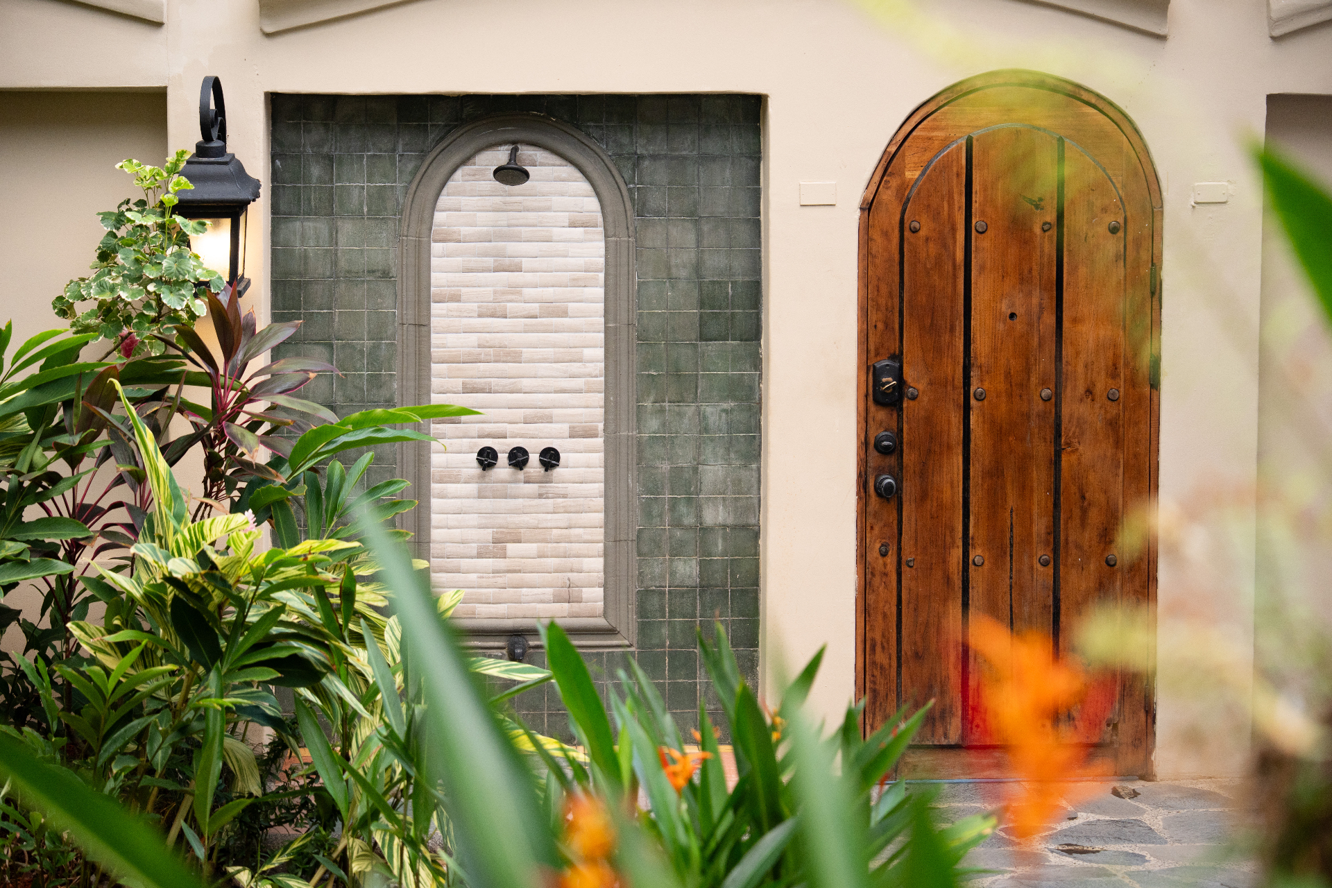 Tiled outdoor shower and arched wooden door framed by tropical planting